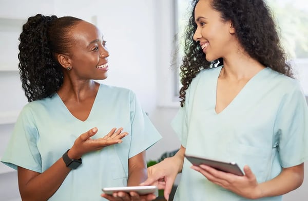 Two female medical professionals smiling and holding tablets.