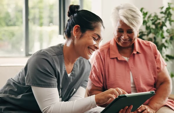 Smiling female nurse with tablet sitting with female patient.
