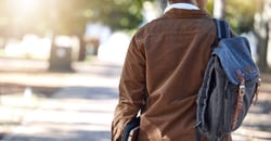 male walking with backpack and school books
