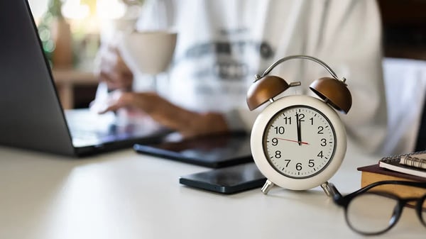 clock on desk with person on laptop
